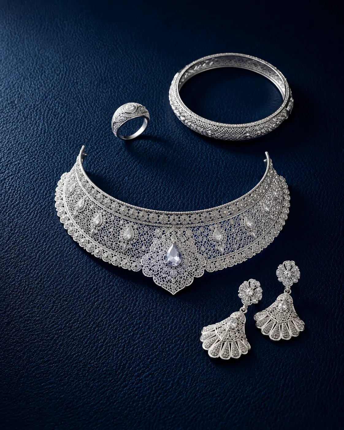 White gold filigree choker with matching earrings, bangle and ring on navy leather